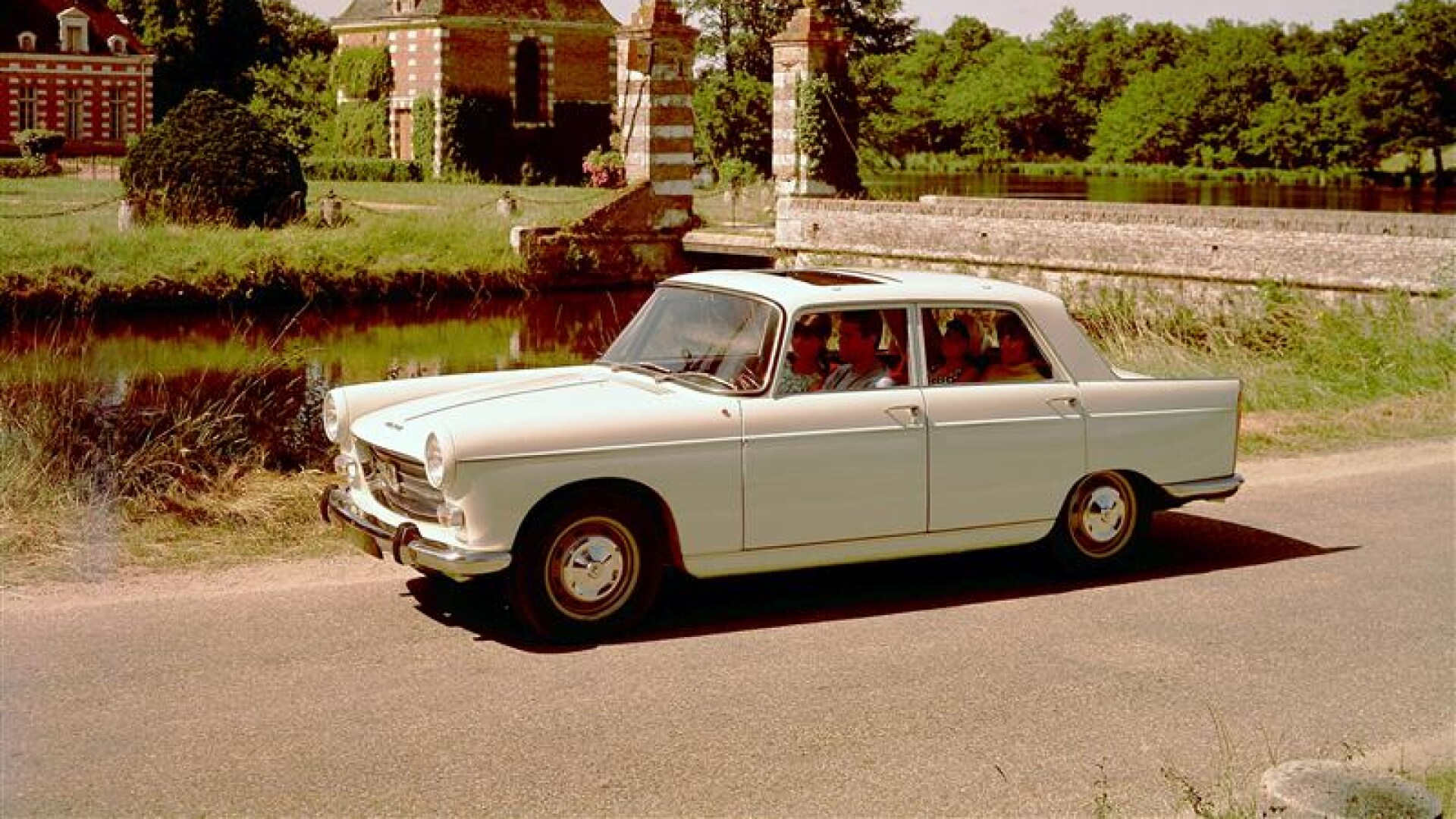 PEUGEOT 404 numa estrada rural em frente a um castelo de tijolos vermelhos e vegetação